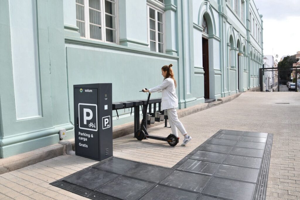 Mujer aparcando un patinete eléctrico en un parking solar para bicicletas y patinetes con pavimento fotovoltaico en Canarias